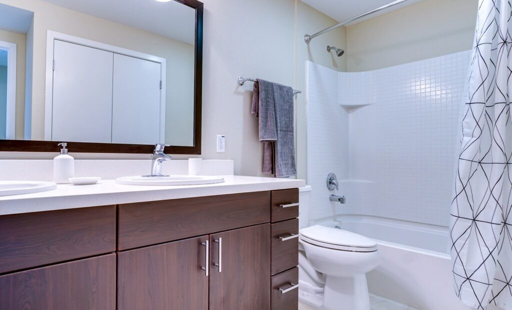 Modern bathroom with a white bathtub and shower, patterned shower curtain, toilet, large mirror, towels on a rack, and dark wood vanity with a sink and soap dispenser.